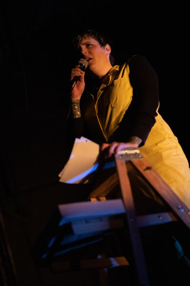 Miriam at the top of a ladder with papers and a microphone