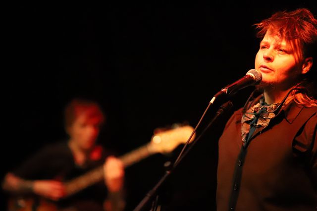 Lars at a mic, in front of Mia playing bass