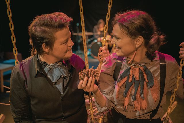 Julie handing Lars a pinecone, as they sit together in yellow swings