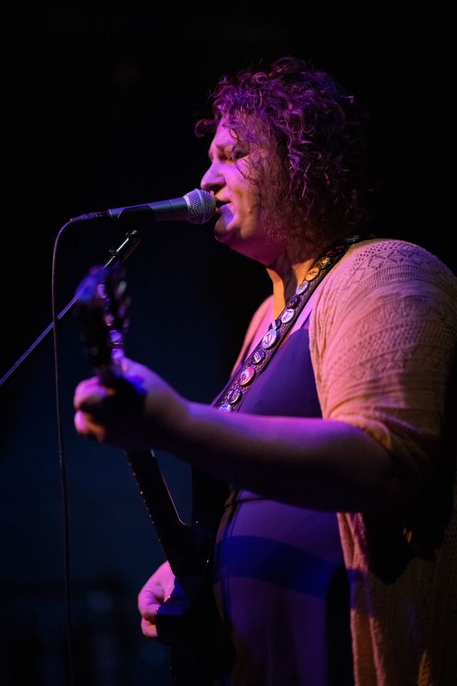 Josie at a mic, sings and plays guitar