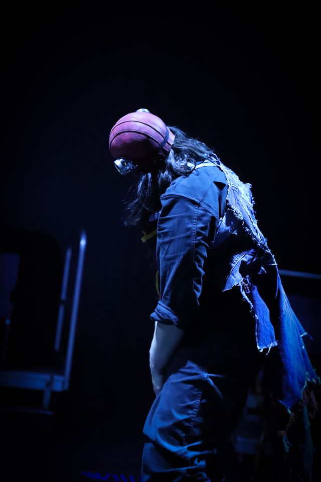 A bower bird dancer in blue light, hunched and facing away