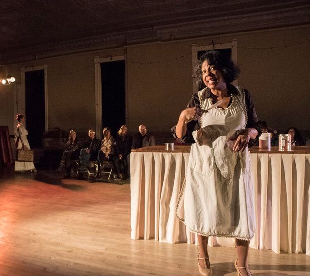 Woman in an apron, dancing and singing into a wooden spoon