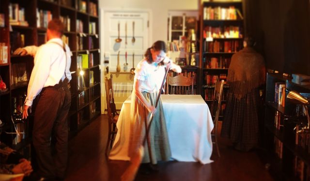 Julie sweeping in front of a table, Meghan and Buba have their backs turned