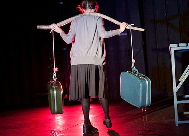 Julie walks away carrying a yoke with two suitcases dripping water
