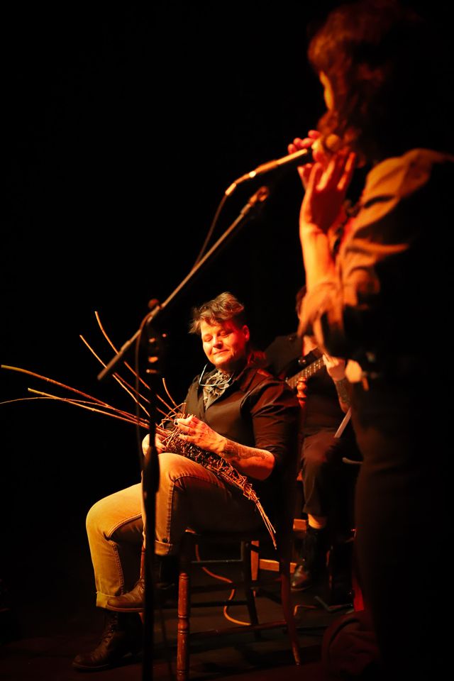 Julie at the mic, singing to Lars who is weaving a cone out of branches