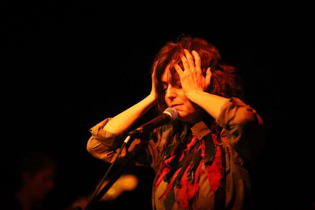 Julie clutching their head in distress at a mic