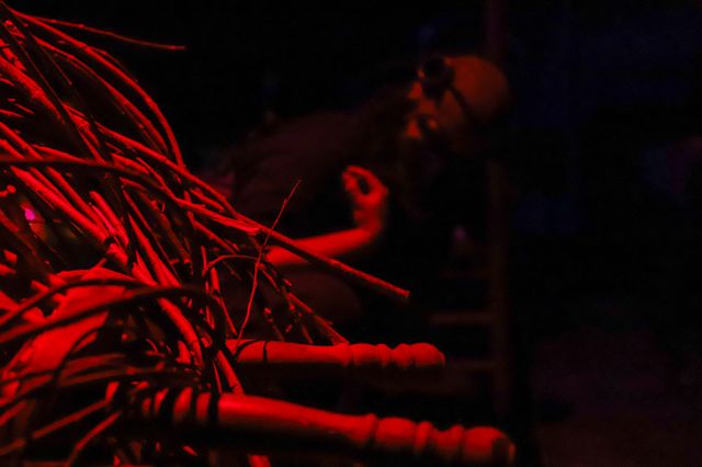 An arm reaches out in twisted gesture from a nest of chairs and branches